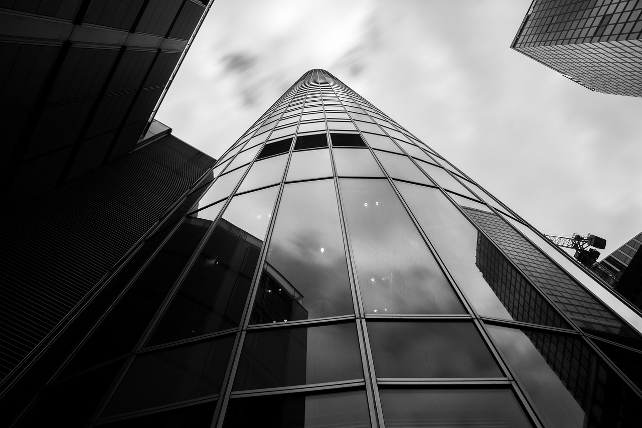 Low-angle black and white view of a tall glass office tower against clouds