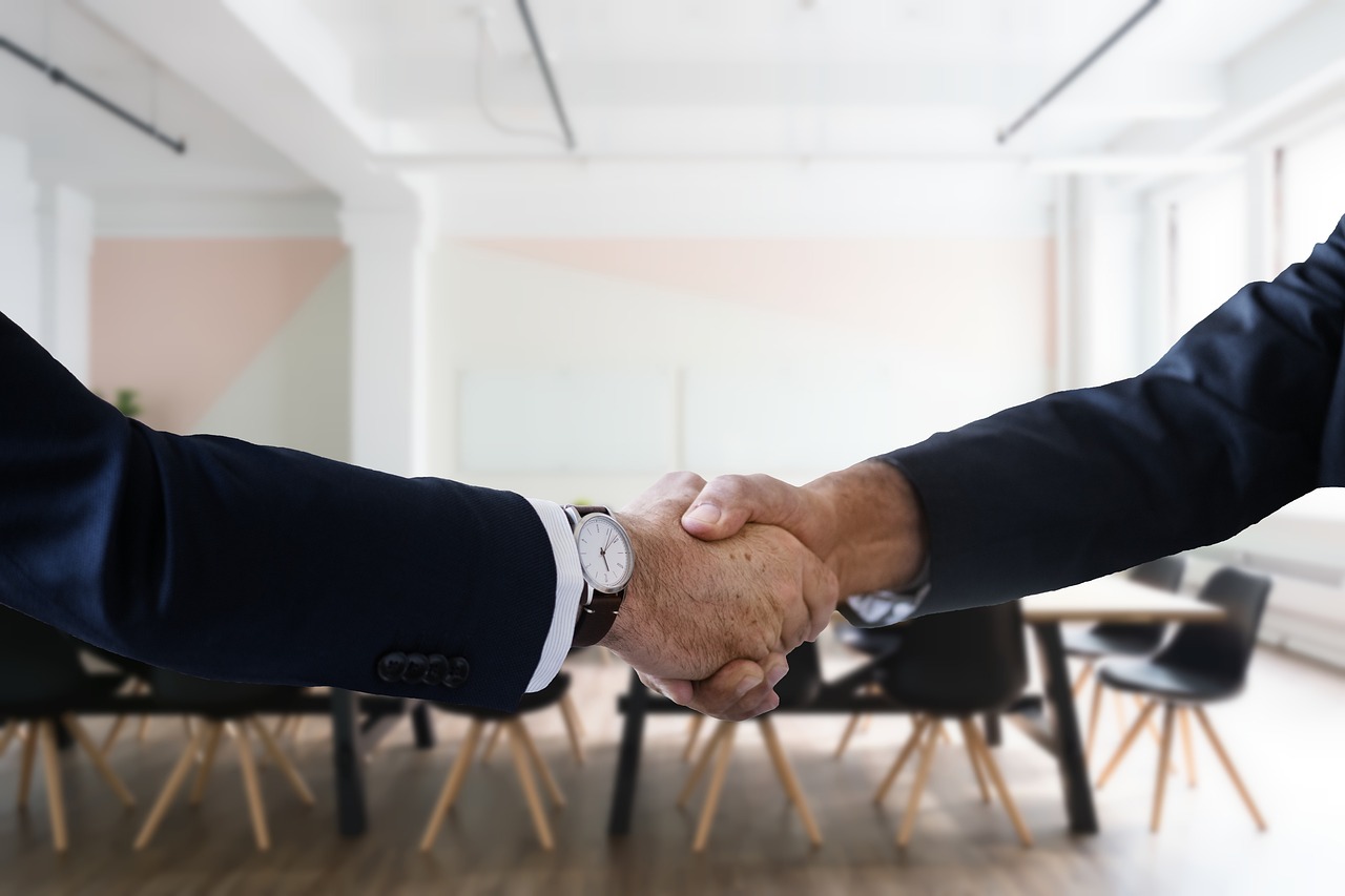 Two people in dark suits shaking hands in an office conference room